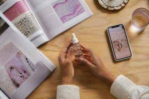 Hands holding a skincare product with research materials on a wooden table